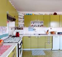 Kuchyně v rodinném domě s olivovými skříňkami, spotřebiči a poličkami s šálky.