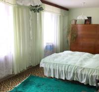 Ložnice v rodinném domě s koberci, záclonami a dřevěnou skříní.