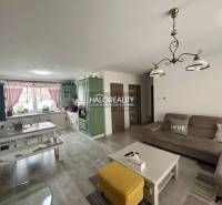 Obývací pokoj v rodinném domě se sedací soupravou, stolem a kuchyňskou linkou.