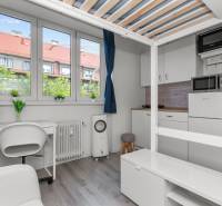 Garsonka s podlahou s dřevěným dekorem, pracovním stolem a kuchyní s mikrovlnnou troubou.