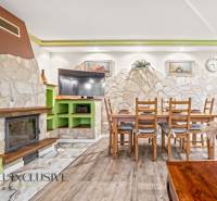 Interiér rodinného domu s krbem, kamennou stěnou, jídelním stolem a podlahou s dřevěným dekorem.