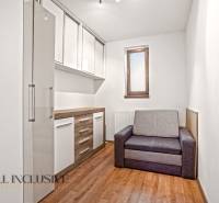 Pokoj v rodinném domě s podlahou s dřevěným dekorem, šedou sedačkou a úložnými skříňkami.