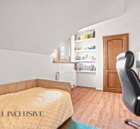 Pokoj v rodinném domě s postelí, policemi, stolem a podlahou s dřevěným dekorem.