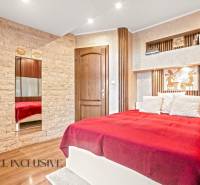 Ložnice v rodinném domě s postelí, kamennými detaily a podlahou s dřevěným dekorem.