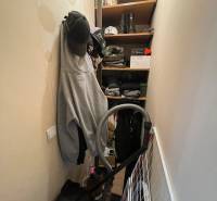 Úložný prostor s oblečením, čepicemi, botami a vysavačem v 1-pokojovém bytě.