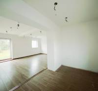 Interiér rodinného domu s podlahou s dřevěným dekorem a velkými okny do zahrady.