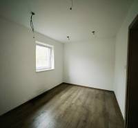 Pokoj v rodinném domě s bílými stěnami a podlahou s dřevěným dekorem.