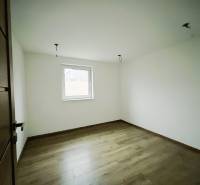 Pokoj v rodinném domě s bílými stěnami a podlahou s dřevěným dekorem.