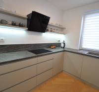 Kuchyně v rodinném domě s tmavou pracovní deskou a podlahou s dřevěným dekorem.