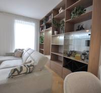 Obývací pokoj v rodinném domě s bílou pohovkou, dřevěnou knihovnou a rostlinami.