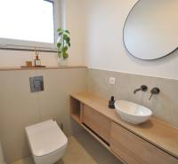 Koupelna v rodinném domě s kulatým zrcadlem, umyvadlem a podlahou s dřevěným dekorem.