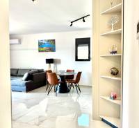 Interiér 1-pokojového bytu s bílou podlahou, šedou pohovkou a jídelním stolem.