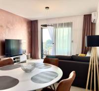 Obývací pokoj v jednopokojovém bytě s televizí, balkonem a elegantním stolem.