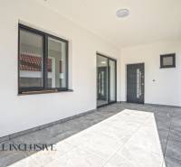 Rodinný dům s terasou, velkými okny a šedou podlahou s dlažbou.