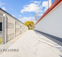 Úzká příjezdová cesta mezi rodinnými domy v Orechové Potôni, lemovaná zdí a stromy.