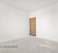 Prázdný pokoj v rodinném domě s bílými stěnami a dveřmi s dřevěným dekorem.