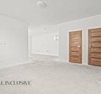 Bílé stěny a dřevěné dveře v interiéru rodinného domu s podlahou bez dekoru.