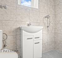 Koupelna v rodinném domě s umyvadlem, sprchou a toaletou ve světlých obkladech.