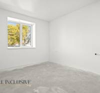 Prázdná místnost v rodinném domě s bílými stěnami a oknem s výhledem na stromy.