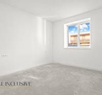 Prázdná místnost s oknem, bílé stěny, výhled na budovu z rodinného domu.