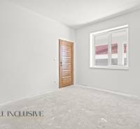 Rodinný dům s bílou stěnou a dřevěnými dveřmi, okno s výhledem na střechu.