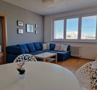 Obývací pokoj 3-pokojového bytu s pohovkou, bílým stolem a podlahou s dřevěným dekorem.