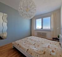 Ložnice v 3-pokojovém bytě s pohodlnou postelí, zrcadlem a podlahou s dřevěným dekorem.