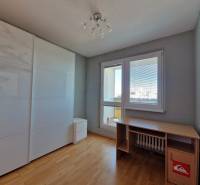 Pokoj v 3-pokojovém bytě s podlahou s dřevěným dekorem, stolem a skříní.