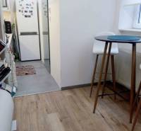 Kuchyně v 1-pokojovém bytě s podlahou s dřevěným dekorem, vysoký stůl a židle.