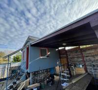 Chata v Komárně na Nové osadě se schodištěm a dřevěným přístřeškem pod oblaky.