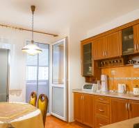 Kuchyně v 2pokojovém bytě s dřevěnými skříňkami, jídelním stolem a vstupem na balkon.