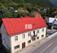 Budova v Belej s červenou střechou na hlavní ulici obklopená zelení a domy.