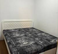 Ložnice v 2pokojovém bytě s postelí, světlými stěnami a podlahou s dřevěným dekorem.