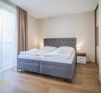 Ložnice v 2pokojovém bytě s pohodlnou postelí, podlahou s dřevěným dekorem a závěsy.