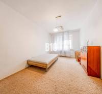 Ložnice ve 4pokojovém bytě s postelí, komodou a kobercem.