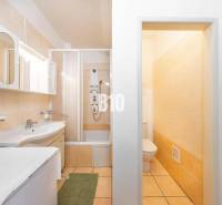 Koupelna ve 4-pokojovém bytě s vanou, skříňkami a toaletou, laděná ve světlých barvách.