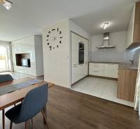 Jídelní prostor ve 4-pokojovém bytě s podlahou s dřevěným dekorem a kuchyní v pozadí.