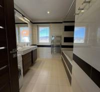 Koupelna ve 4-pokojovém bytě s vanou, umyvadly a pračkou.