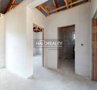 Interiér rodinného domu s neomítnutými stěnami a viditelnou střešní konstrukcí.