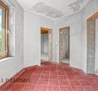 Rodinný dům s červenou dlažbou, omítnuté stěny a tři otevřené průchody.