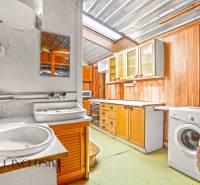 Kuchyně v rodinném domě s dřevěnými skříňkami, dřezem a pračkou.