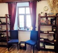 Knihovny s dekoracemi, židle a okno s bordovými závěsy v obchodním prostoru.