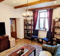 Obývací pokoj s podlahou s dřevěným dekorem, televizorem, policemi a pohodlným nábytkem.