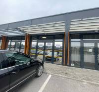 Obchodní prostory na Brněnské ulici v Trenčíně se skleněnou fasádou a parkovištěm.