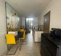 Obchodní prostory s jídelním stolem, žlutými židlemi a kuchyňkou.