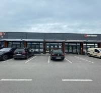 Obchodní prostory na Brněnské ulici v Trenčíně s parkovištěm před prodejnami.