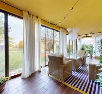 Zimní zahrada v rodinném domě s proutěným nábytkem a výhledem na zahradu.