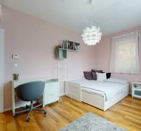 Ložnice v rodinném domě s psacím stolem, postelí a podlahou s dřevěným dekorem.