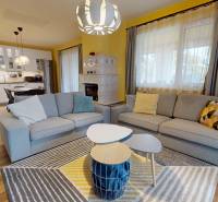 Obývací pokoj v rodinném domě s podlahou s dřevěným dekorem, sedačkami a kuchyní v pozadí.