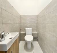 Toaleta s šedými obklady a umyvadlem v kanceláři.